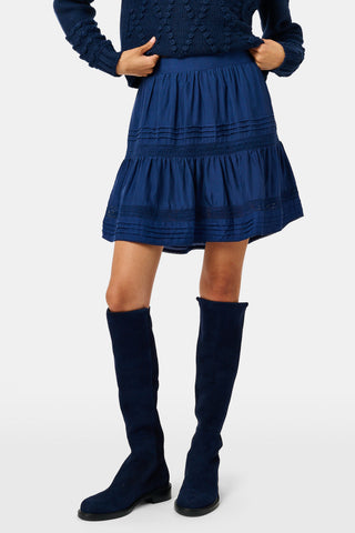 A person wearing a navy tiered silk Fleet Skirt by SOPHISTICA and knee-high suede boots.