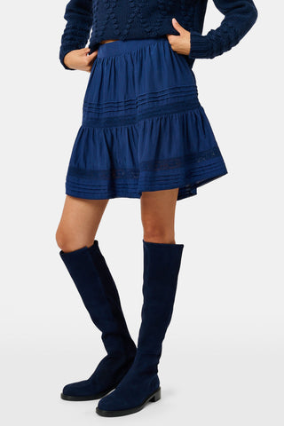 A person wearing a navy tiered silk Fleet Skirt by SOPHISTICA and knee-high suede boots.