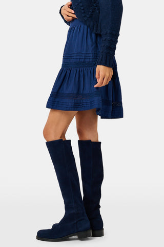 A person wearing a navy tiered silk Fleet Skirt by SOPHISTICA and knee-high suede boots.
