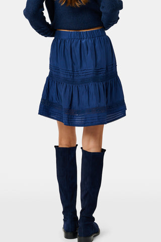 A person wearing a navy tiered silk Fleet Skirt by SOPHISTICA and knee-high suede boots.