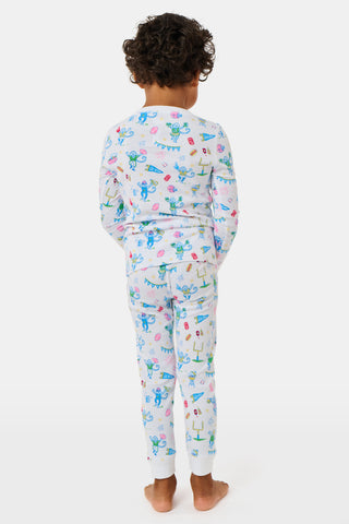 The Kids Game Day Pajamas by Roller Rabbit are a children’s long-sleeve pajama set crafted from soft Pima cotton, featuring a vibrant party-themed print with colorful dinosaurs, bunting, gifts, and party hats on a white background.