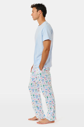 The Mens Game Day Troy Pajamas set by Roller Rabbit features a light blue short-sleeve t-shirt paired with white pajama pants decorated with colorful, playful cartoon animal and toy prints. The set is displayed on a plain white background.
