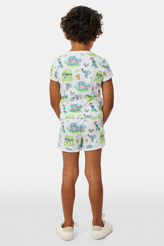A girl stands outdoors in a Roller Rabbit Kids Game, Set, Monkey Playa Play Set, holding out a tennis ball toward the camera. Her playful outfit is perfect for kids’ tennis activities, and the photo is taken from a low angle with blue sky and trees in the background.