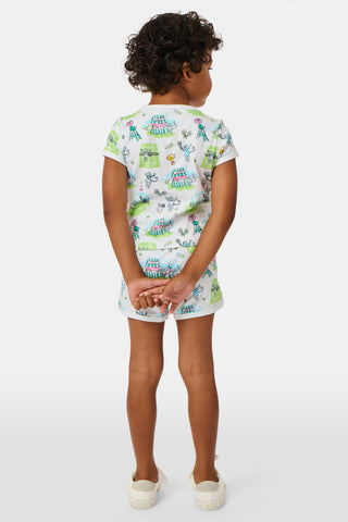 A girl stands outdoors in a Roller Rabbit Kids Game, Set, Monkey Playa Play Set, holding out a tennis ball toward the camera. Her playful outfit is perfect for kids’ tennis activities, and the photo is taken from a low angle with blue sky and trees in the background.