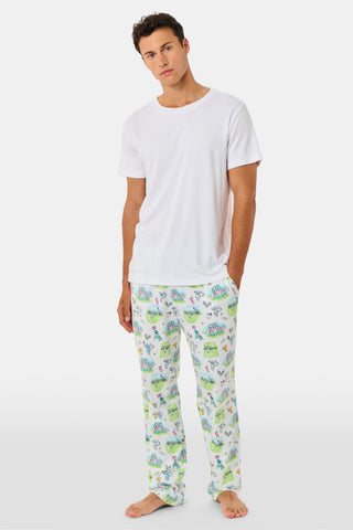 The Roller Rabbit Mens Game, Set, Monkey Troy Pajamas feature a white short-sleeve t-shirt paired with white pajama pants decorated with a vibrant dinosaur and jungle print in green, blue, and black. This playful Pima cotton loungewear set from Roller Rabbit is displayed on a plain white background.