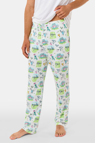 The Roller Rabbit Mens Game, Set, Monkey Troy Pajamas feature a white short-sleeve t-shirt paired with white pajama pants decorated with a vibrant dinosaur and jungle print in green, blue, and black. This playful Pima cotton loungewear set from Roller Rabbit is displayed on a plain white background.