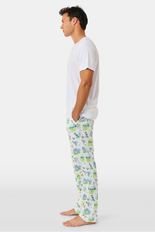 The Roller Rabbit Mens Game, Set, Monkey Troy Pajamas feature a white short-sleeve t-shirt paired with white pajama pants decorated with a vibrant dinosaur and jungle print in green, blue, and black. This playful Pima cotton loungewear set from Roller Rabbit is displayed on a plain white background.