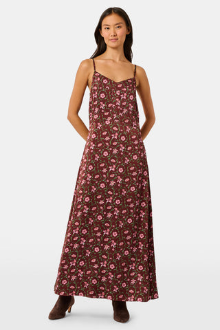 A woman wears a brown silk satin Greta Floral Ditsy Alice Dress with a sweetheart neckline, pink floral ditsy print, and thin straps, paired with brown ankle boots.