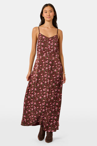 A woman wears a brown silk satin Greta Floral Ditsy Alice Dress with a sweetheart neckline, pink floral ditsy print, and thin straps, paired with brown ankle boots.