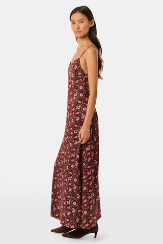 A woman wears a brown silk satin Greta Floral Ditsy Alice Dress with a sweetheart neckline, pink floral ditsy print, and thin straps, paired with brown ankle boots.