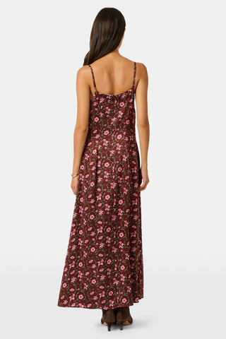 A woman wears a brown silk satin Greta Floral Ditsy Alice Dress with a sweetheart neckline, pink floral ditsy print, and thin straps, paired with brown ankle boots.