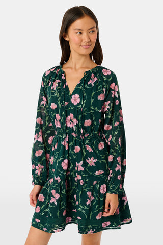 A model wears the SOPHISTICA Greta Floral Belle Dress, a dark green cotton mini dress featuring a pink floral print, a gathered waist, and a ruffled hem.