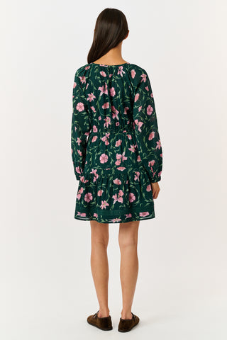 A model wears the SOPHISTICA Greta Floral Belle Dress, a dark green cotton mini dress featuring a pink floral print, a gathered waist, and a ruffled hem.