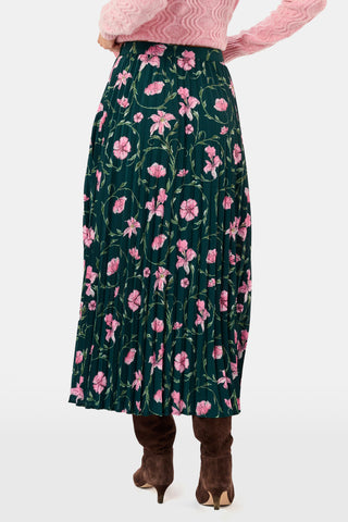 The SOPHISTICA Greta Floral Megan Skirt is a midi-length pleated skirt featuring a dark green background with a pink floral pattern, worn with a pink cable-knit sweater and brown suede ankle boots.