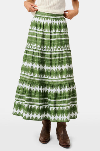 A person wearing the Roller Rabbit Hayam Carlisa Skirt in an olive and white print, paired with a cream knit top and brown boots, stands against a plain white background.