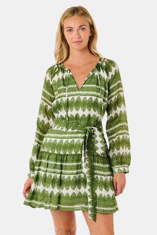 A woman outdoors wears the Hayam Monroe Dress by Roller Rabbit—an olive and white long-sleeved dress with a matching belt. She walks with another person, with trees and a wooden fence in the background.