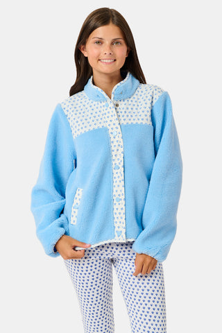A young girl stands and smiles against a plain background, wearing the Roller Rabbit Kids Hearts Lizzie Fleece Jacket in light blue with white patterned details, paired with matching white leggings adorned with blue hearts. This cozy outerwear features soft fleece for comfort and warmth.