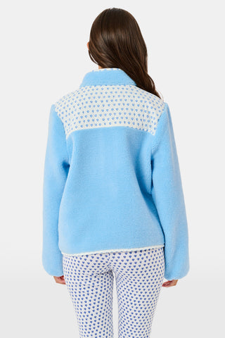 A young girl stands and smiles against a plain background, wearing the Roller Rabbit Kids Hearts Lizzie Fleece Jacket in light blue with white patterned details, paired with matching white leggings adorned with blue hearts. This cozy outerwear features soft fleece for comfort and warmth.