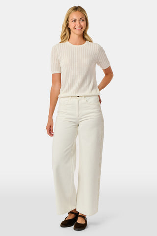 A woman wearing the Roller Rabbit Chain Pointelle Lauren Sweater in cream and white pants, standing against a white background.