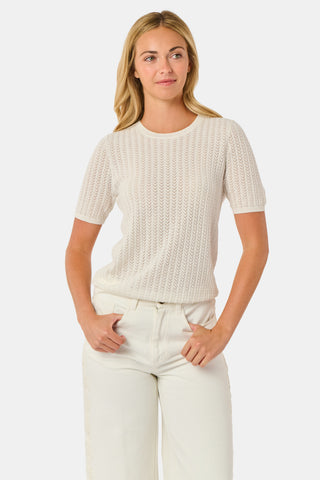 A woman wearing the Roller Rabbit Chain Pointelle Lauren Sweater in cream and white pants, standing against a white background.