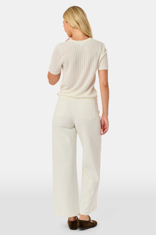 A woman wearing the Roller Rabbit Chain Pointelle Lauren Sweater in cream and white pants, standing against a white background.