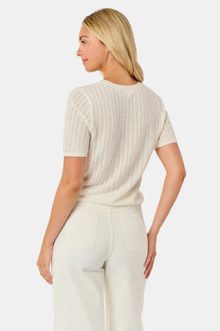 A woman wearing the Roller Rabbit Chain Pointelle Lauren Sweater in cream and white pants, standing against a white background.