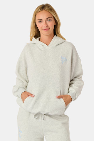 A person is wearing the Roller Rabbit Sleep Club Mimi Sweatpants in light gray, featuring wide legs and crafted from velvety soft Dream Fleece with “Sleep Club” printed in light blue on the left thigh, paired with white sneakers and a cropped white top. The background is plain white.