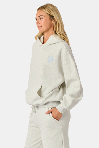 A person is wearing the Roller Rabbit Sleep Club Mimi Sweatpants in light gray, featuring wide legs and crafted from velvety soft Dream Fleece with “Sleep Club” printed in light blue on the left thigh, paired with white sneakers and a cropped white top. The background is plain white.