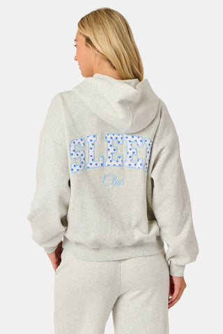 A person is wearing the Roller Rabbit Sleep Club Mimi Sweatpants in light gray, featuring wide legs and crafted from velvety soft Dream Fleece with “Sleep Club” printed in light blue on the left thigh, paired with white sneakers and a cropped white top. The background is plain white.