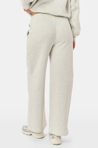 A person is wearing the Roller Rabbit Sleep Club Mimi Sweatpants in light gray, featuring wide legs and crafted from velvety soft Dream Fleece with “Sleep Club” printed in light blue on the left thigh, paired with white sneakers and a cropped white top. The background is plain white.
