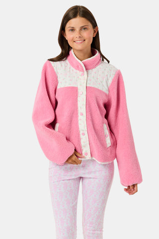 A young girl smiles, wearing the Roller Rabbit Kids Mini Monkey Blossom Lizzie Fleece Jacket, featuring white patterned panels, and matching pink leggings with colorful fruit prints, standing against a plain light gray background.