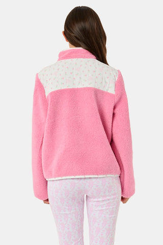 A young girl smiles, wearing the Roller Rabbit Kids Mini Monkey Blossom Lizzie Fleece Jacket, featuring white patterned panels, and matching pink leggings with colorful fruit prints, standing against a plain light gray background.