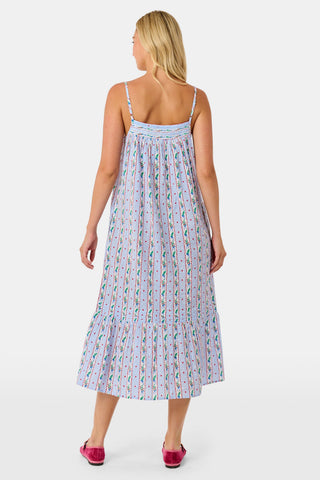 A woman wears a sleeveless SANSKRITI Mistletoe Stripe Augustine Dress in cotton with vertical floral patterns and a ruffled hem, paired with pink flat shoes.