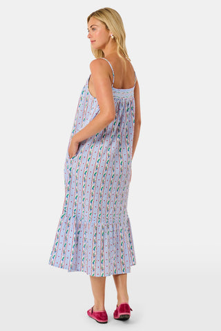 A woman wears a sleeveless SANSKRITI Mistletoe Stripe Augustine Dress in cotton with vertical floral patterns and a ruffled hem, paired with pink flat shoes.
