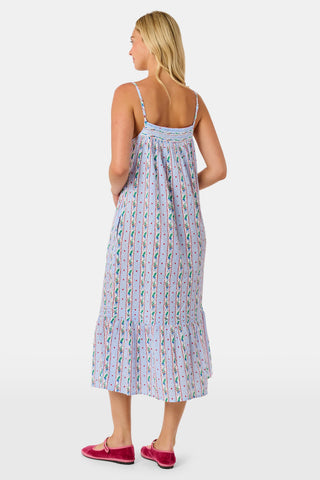 A woman wears a sleeveless SANSKRITI Mistletoe Stripe Augustine Dress in cotton with vertical floral patterns and a ruffled hem, paired with pink flat shoes.