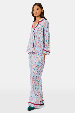 A person wearing a Mistletoe Stripe Josie Loungewear set with red trim, a matching sleep mask, and dark socks, sitting on a mossy tree trunk.