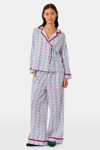 A person wearing a Mistletoe Stripe Josie Loungewear set with red trim, a matching sleep mask, and dark socks, sitting on a mossy tree trunk.