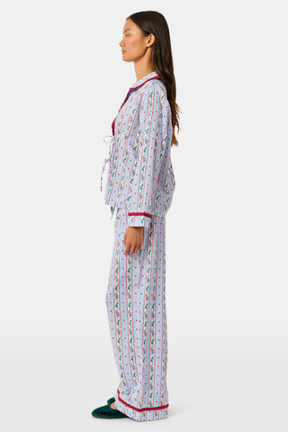 A person wearing a Mistletoe Stripe Josie Loungewear set with red trim, a matching sleep mask, and dark socks, sitting on a mossy tree trunk.