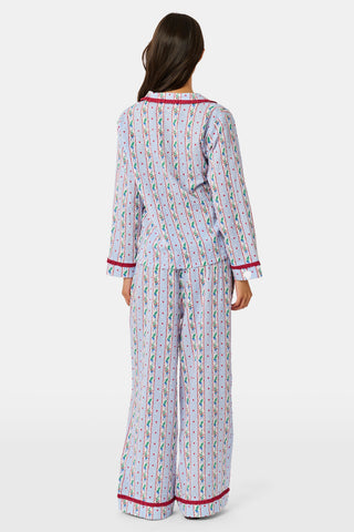 A person wearing a Mistletoe Stripe Josie Loungewear set with red trim, a matching sleep mask, and dark socks, sitting on a mossy tree trunk.