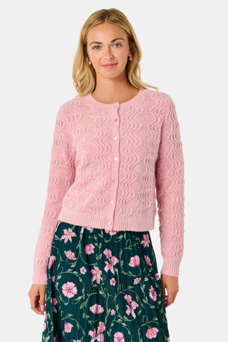 A woman wearing an AFFINA Wave Knit Moxie Cardigan in light pink over a dark green pleated skirt with a pink floral print.