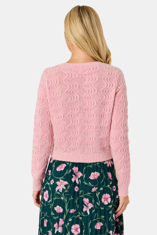 A woman wearing an AFFINA Wave Knit Moxie Cardigan in light pink over a dark green pleated skirt with a pink floral print.