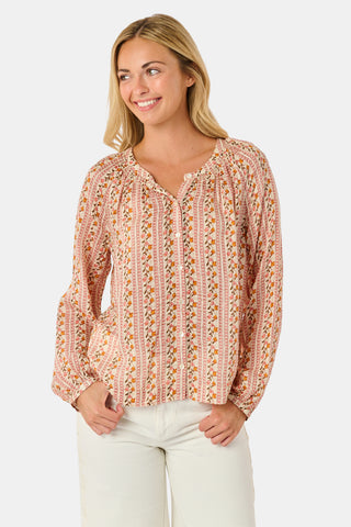A woman stands smiling with one hand in her pocket against a plain white background, wearing the Roller Rabbit Priya Floral Colleen Top.