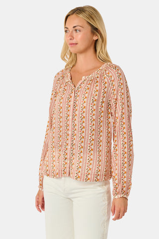 A woman stands smiling with one hand in her pocket against a plain white background, wearing the Roller Rabbit Priya Floral Colleen Top.