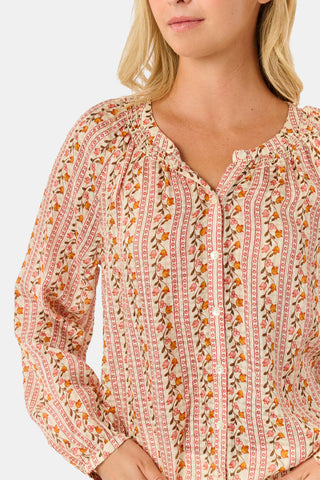 A woman stands smiling with one hand in her pocket against a plain white background, wearing the Roller Rabbit Priya Floral Colleen Top.