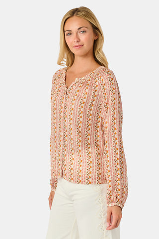 A woman stands smiling with one hand in her pocket against a plain white background, wearing the Roller Rabbit Priya Floral Colleen Top.