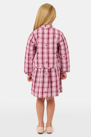 A young girl wearing a pink and white plaid hearts Kids Plaid Hearts Finn Jacket and a matching skirt.