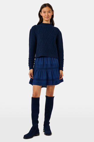 A person wearing a navy tiered silk Fleet Skirt by SOPHISTICA and knee-high suede boots.