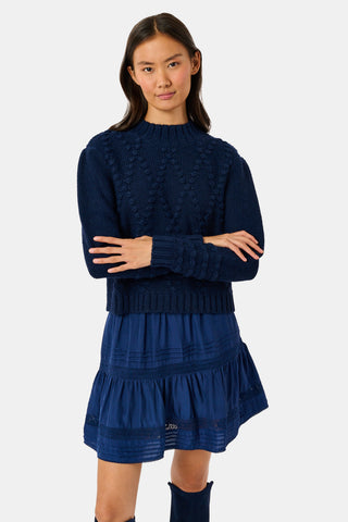 A person wearing a navy blue REVOLUTION KNITS Popcorn Knit Tessa Sweater featuring a textured, popcorn-stitch diamond pattern and a mock-neck.