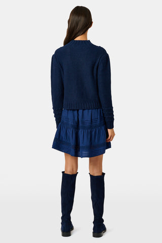 A person wearing a navy blue REVOLUTION KNITS Popcorn Knit Tessa Sweater featuring a textured, popcorn-stitch diamond pattern and a mock-neck.