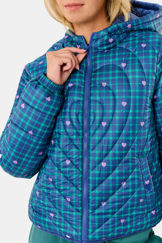 A woman wearing a SOPHISTICA Plaid Hearts Reversible Puffer Jacket, a hooded, zip-front nylon puffer in an emerald green and blue plaid pattern accented by small pink hearts.
